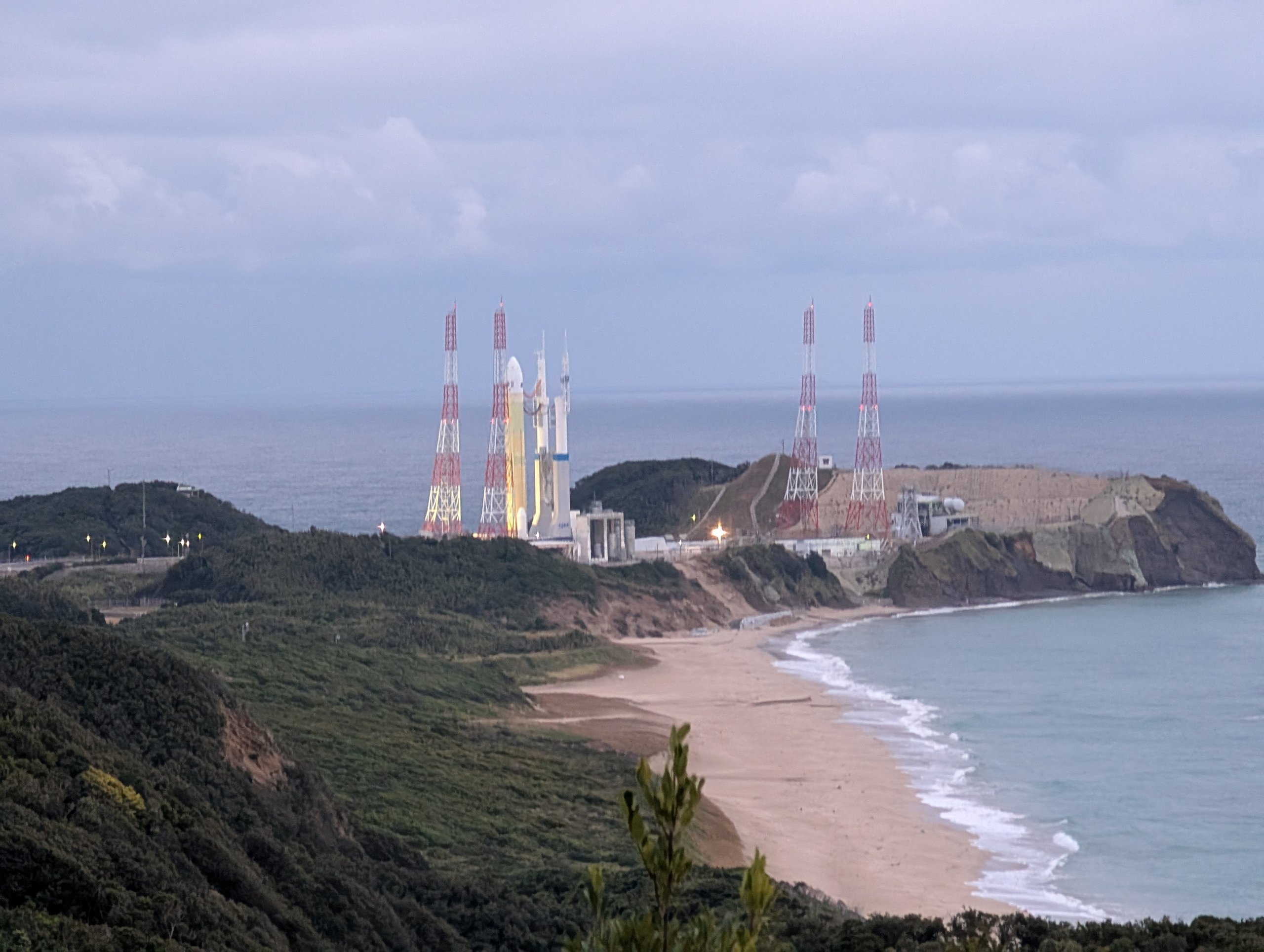 入り江と砂浜の向こうの岬に立つ、発射台とロケット