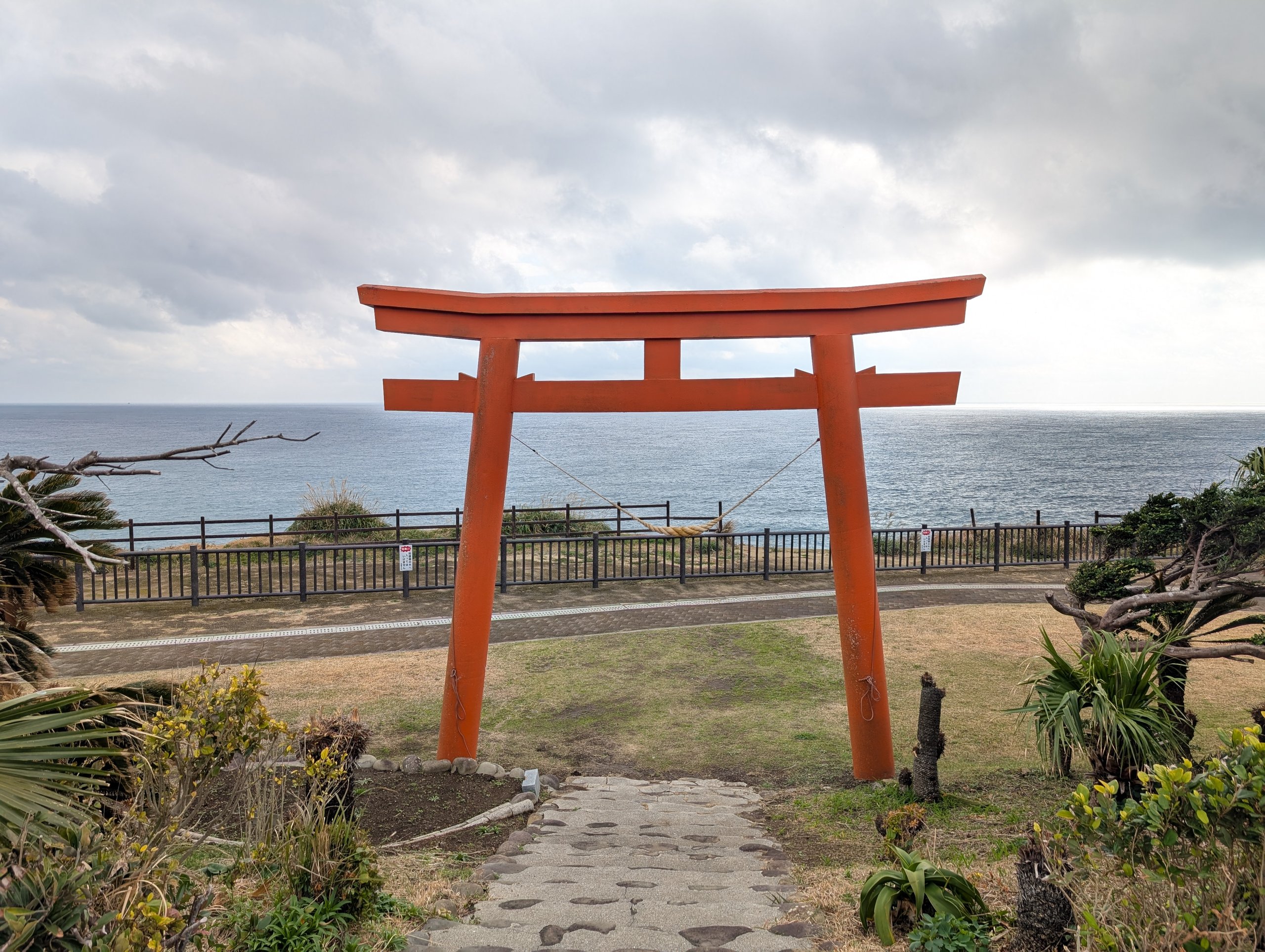 海を背にして立つ朱色の鳥居と、石畳の道