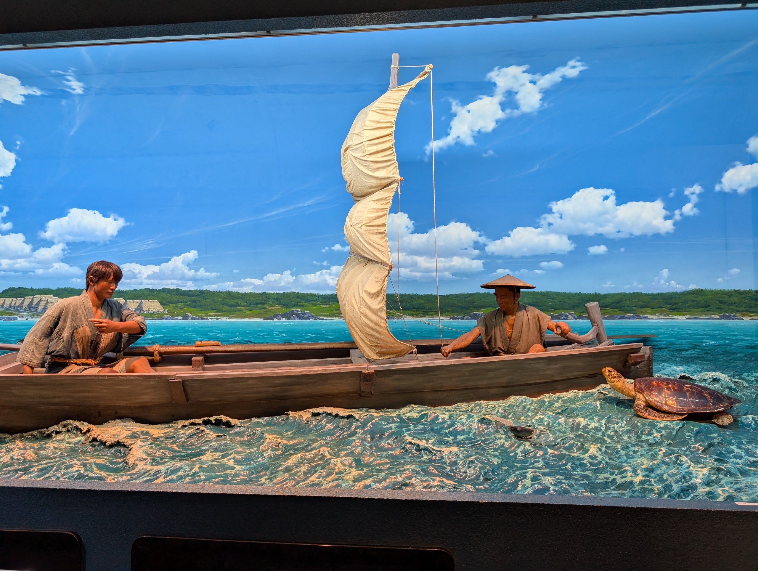小舟に乗った人の人形と帆を再現した、海辺の場面の展示