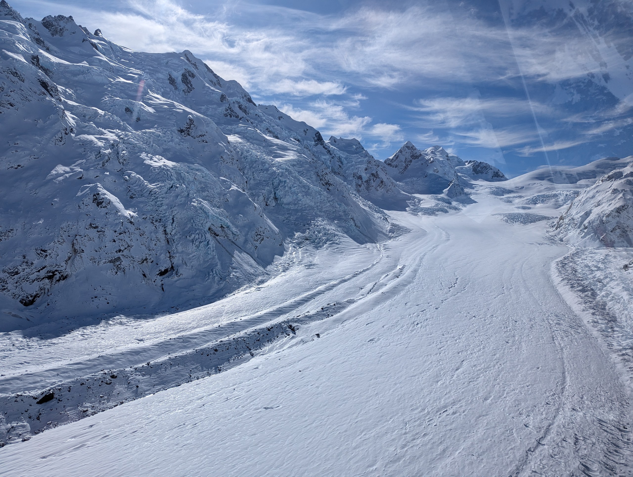ヘリの窓から見た、雪山の間をカーブしながら奥へ続く真っ白な氷河