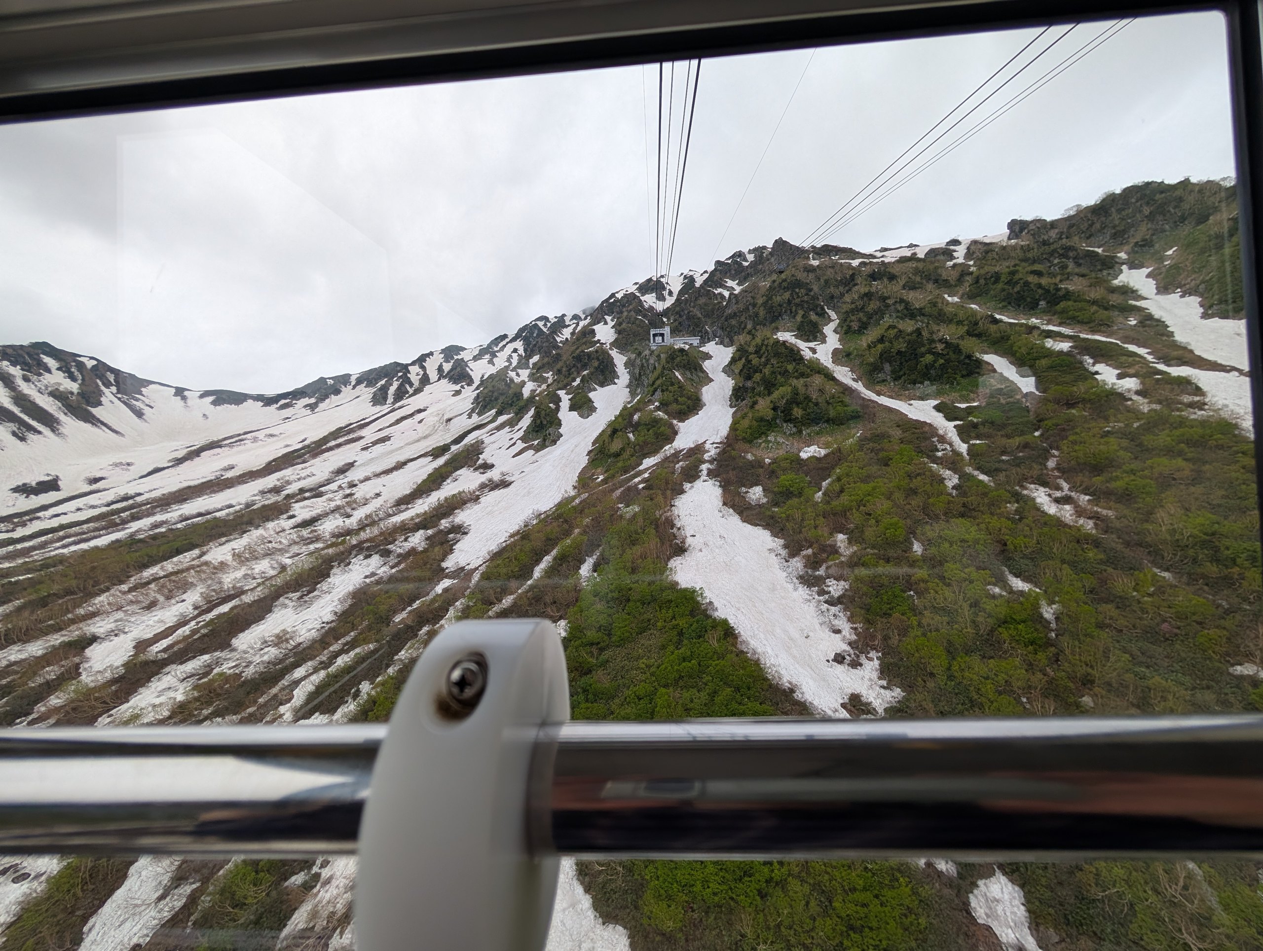 ロープウェイの窓から見た、雪の残る山の斜面