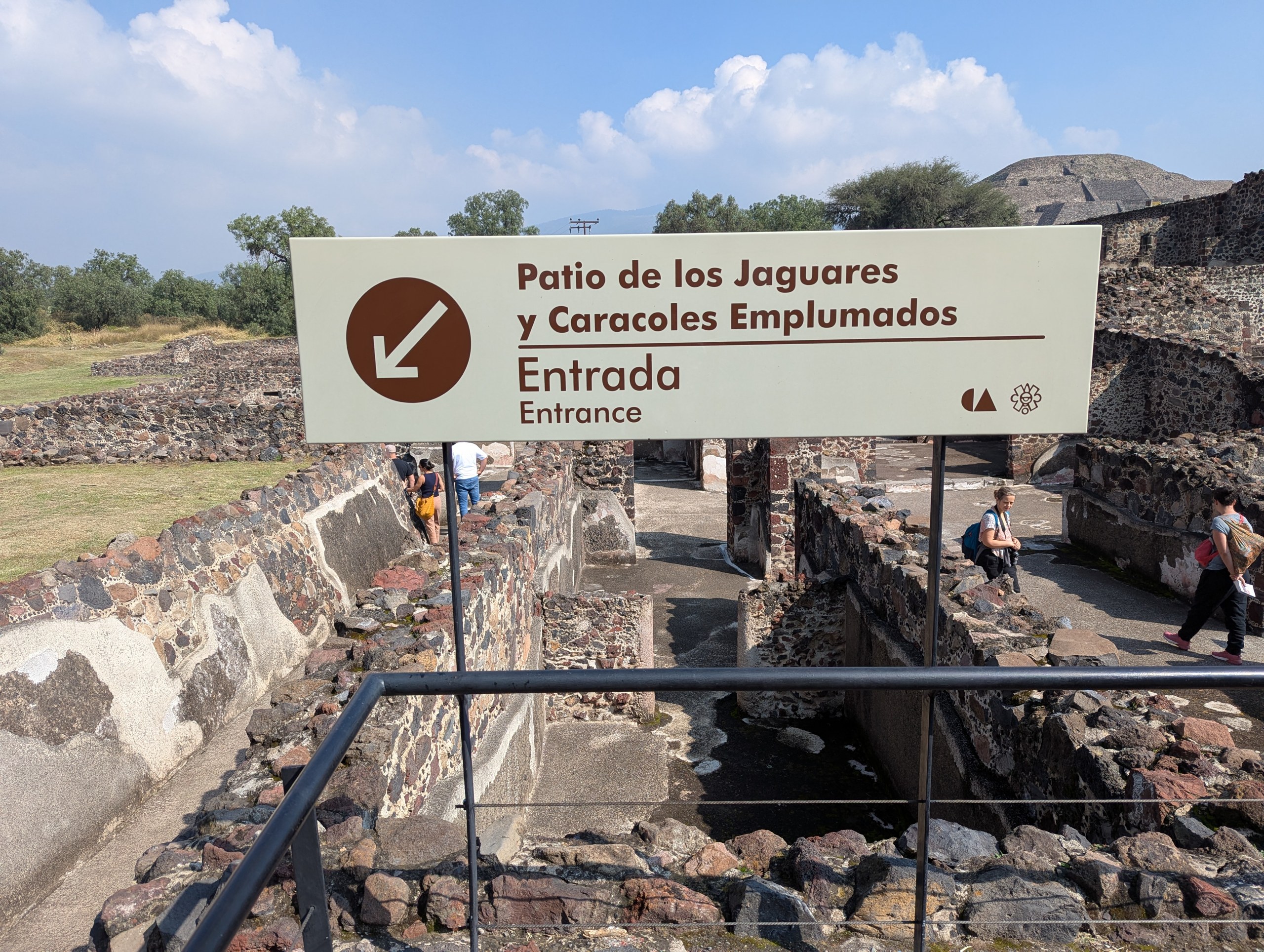「Patio de los Jaguares y Caracoles Emplumados」の入口の看板と、その奥の石積みの遺構