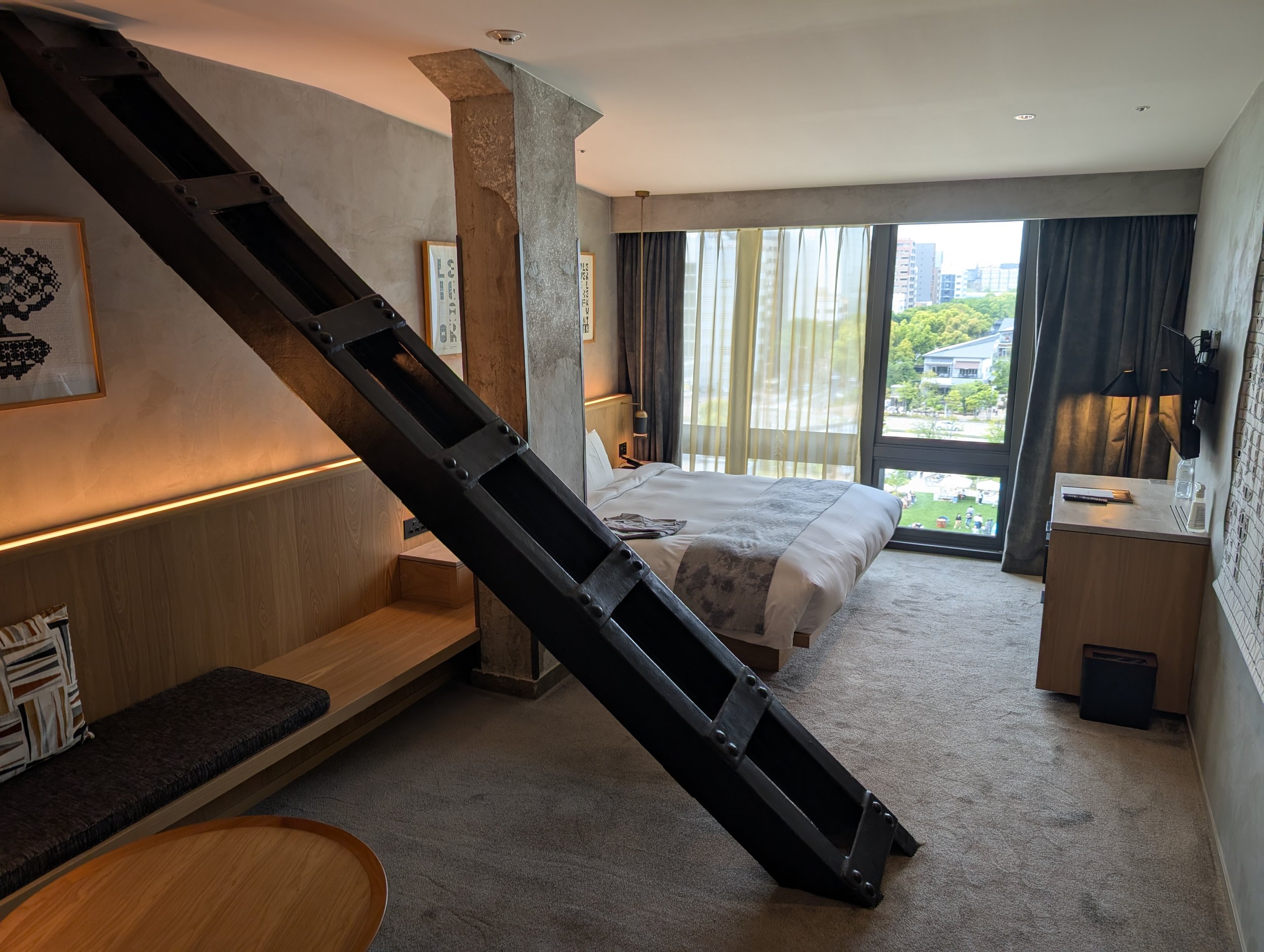 部屋の中を斜めに通る黒い鉄骨と、奥のベッドと窓