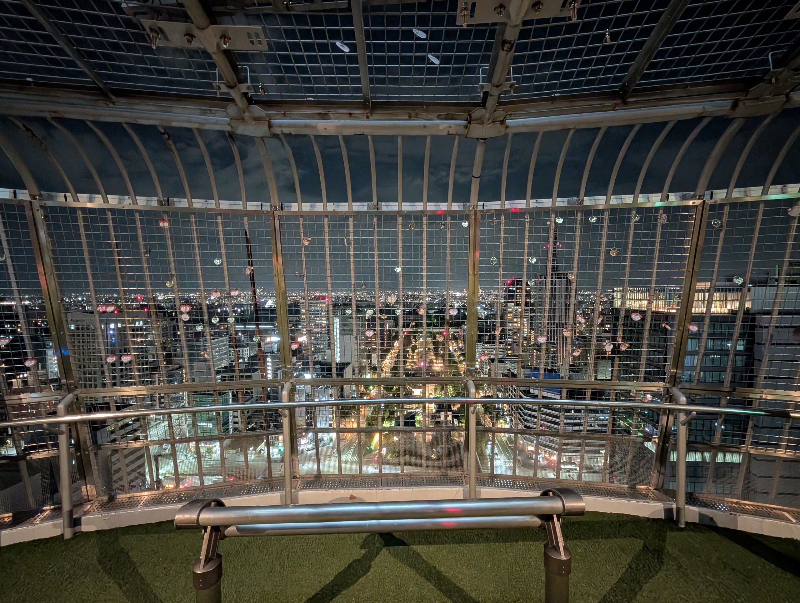 網目の柵に囲まれた夜の展望台と、その向こうの街の明かり