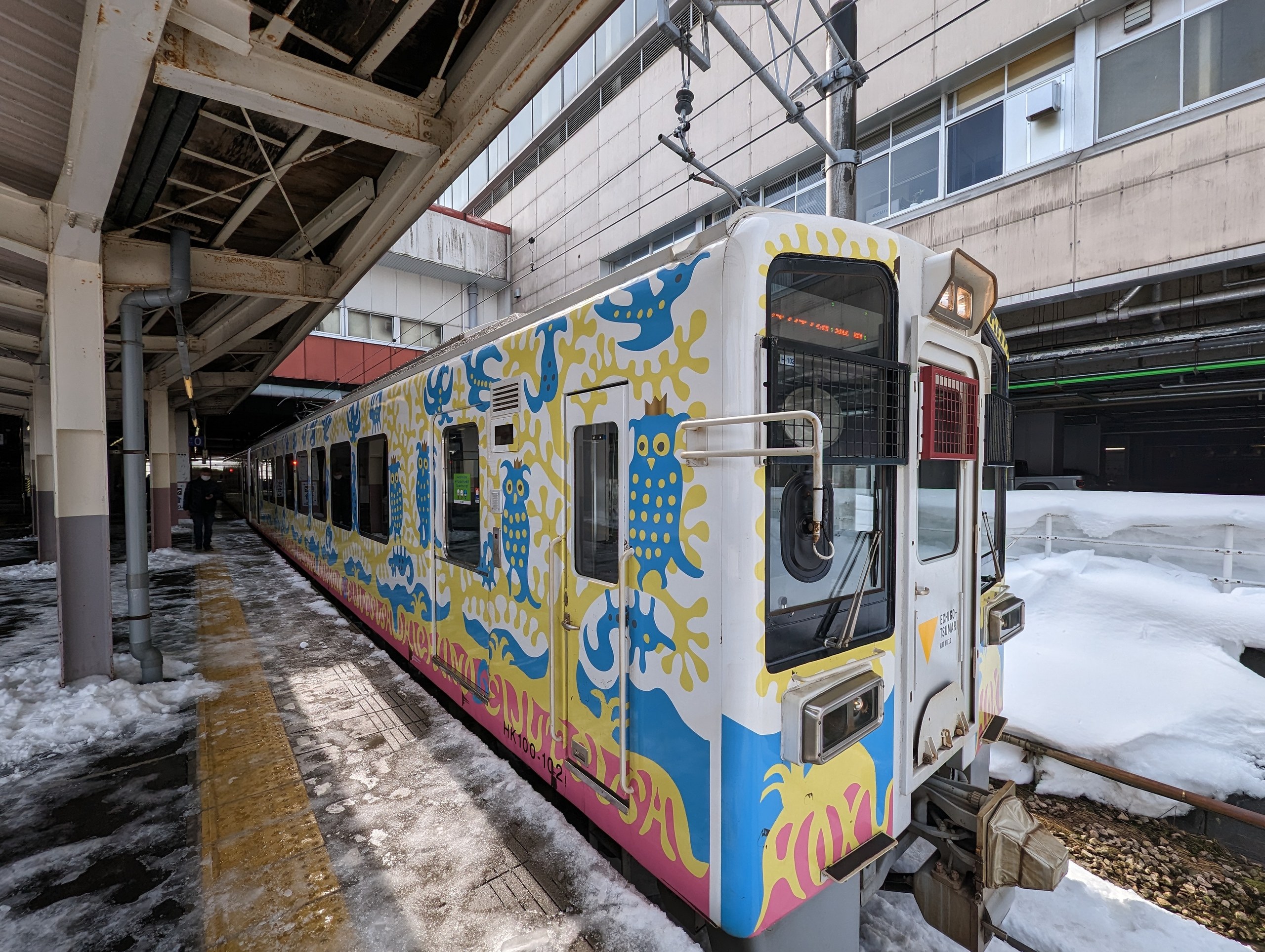 雪の残るホームに停まる、カラフルな絵が描かれた電車