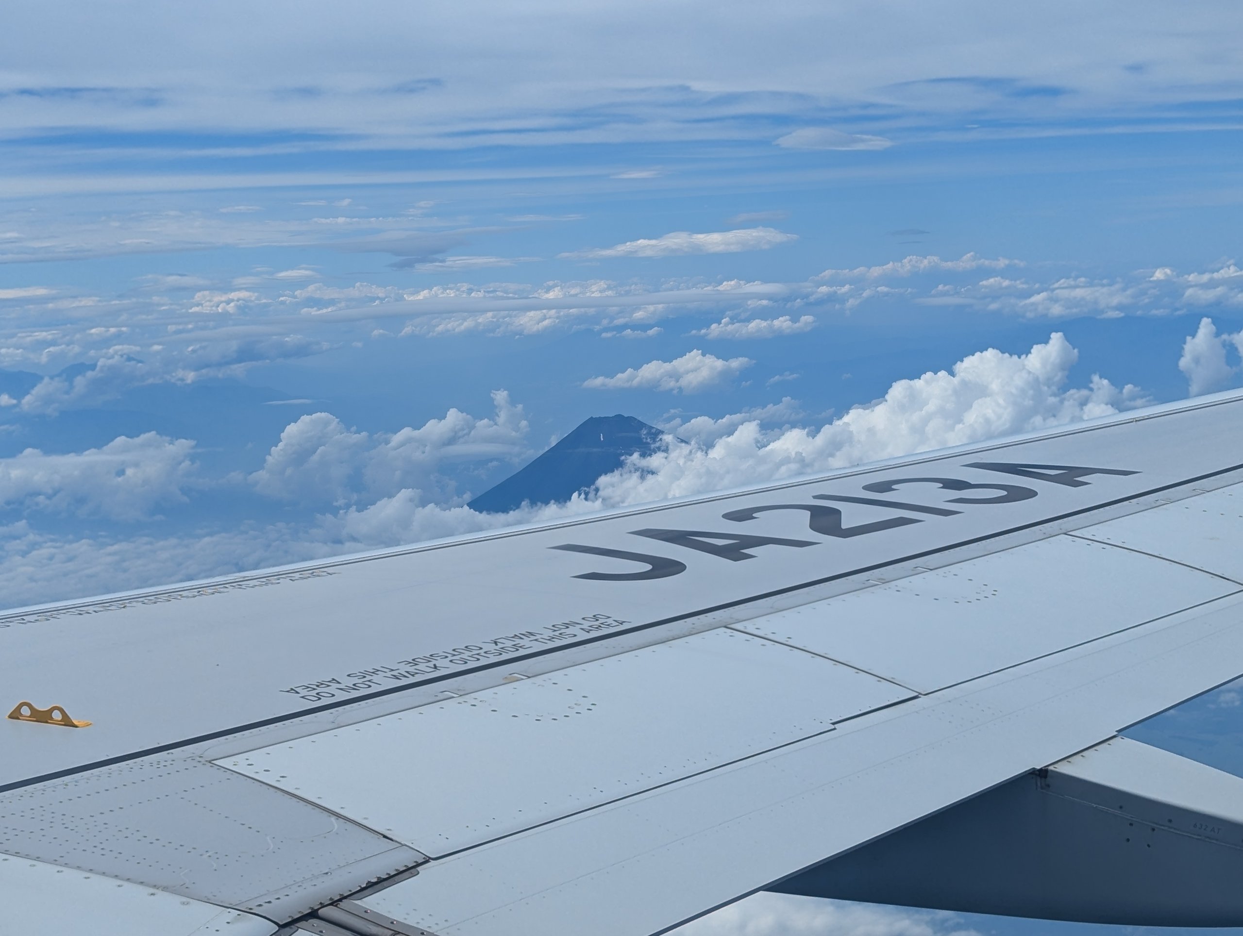 飛行機の窓から見た、雲の上の富士山と主翼