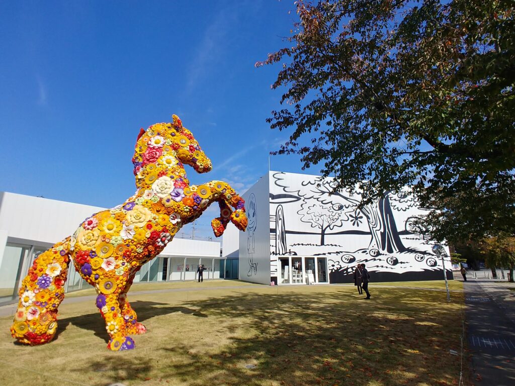 十和田市現代美術館の前に立つ、花で覆われた馬の作品「フラワー・ホース」