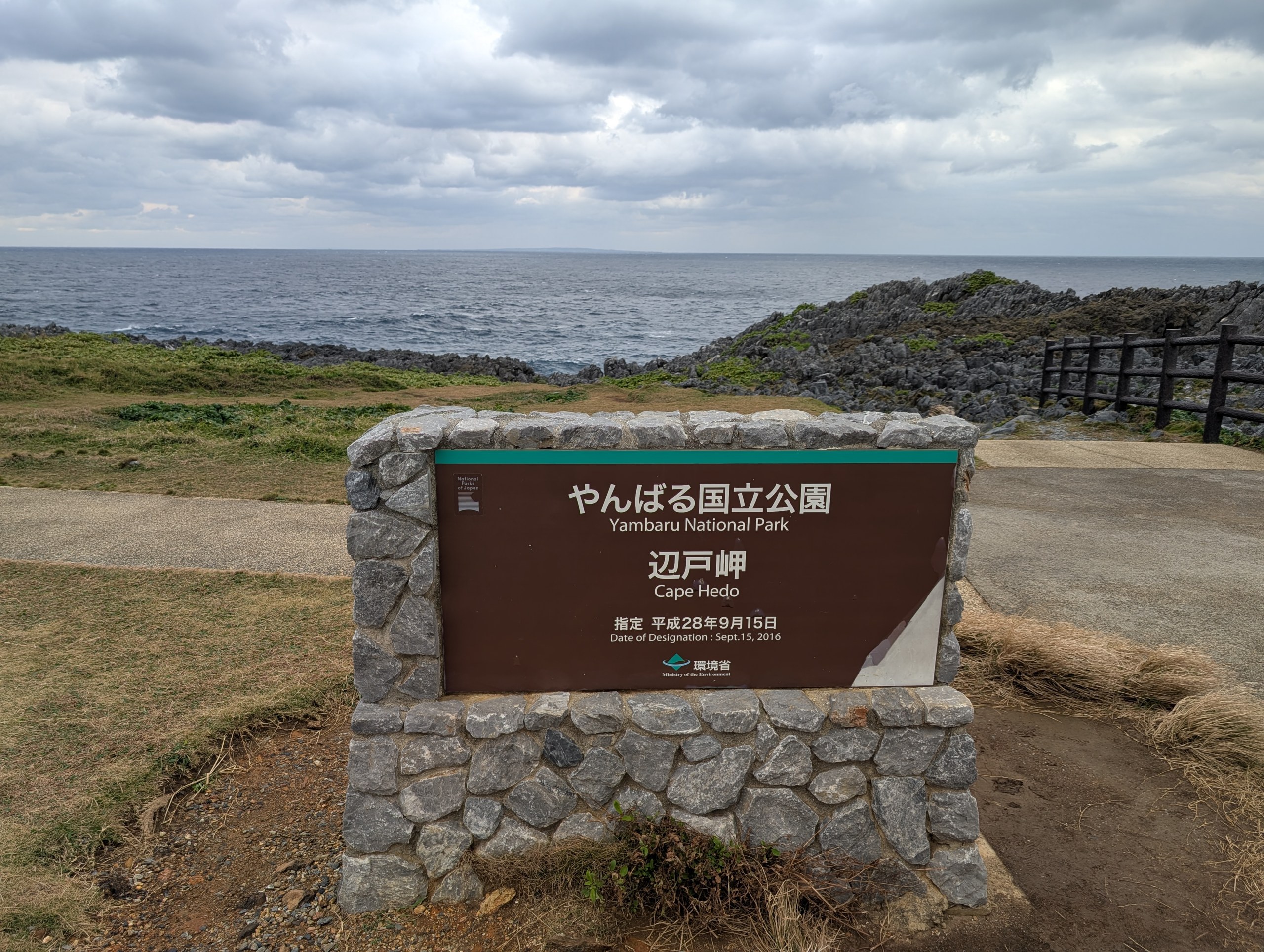 石積みの台の上の「やんばる国立公園 辺戸岬」の看板。後ろに海と岩場